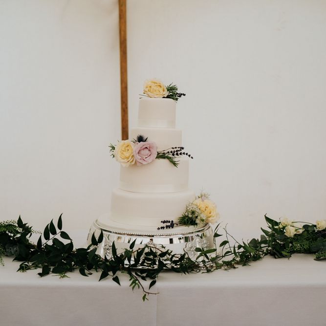 Three-tiered, white wedding cake with yellow and pink roses as decoration