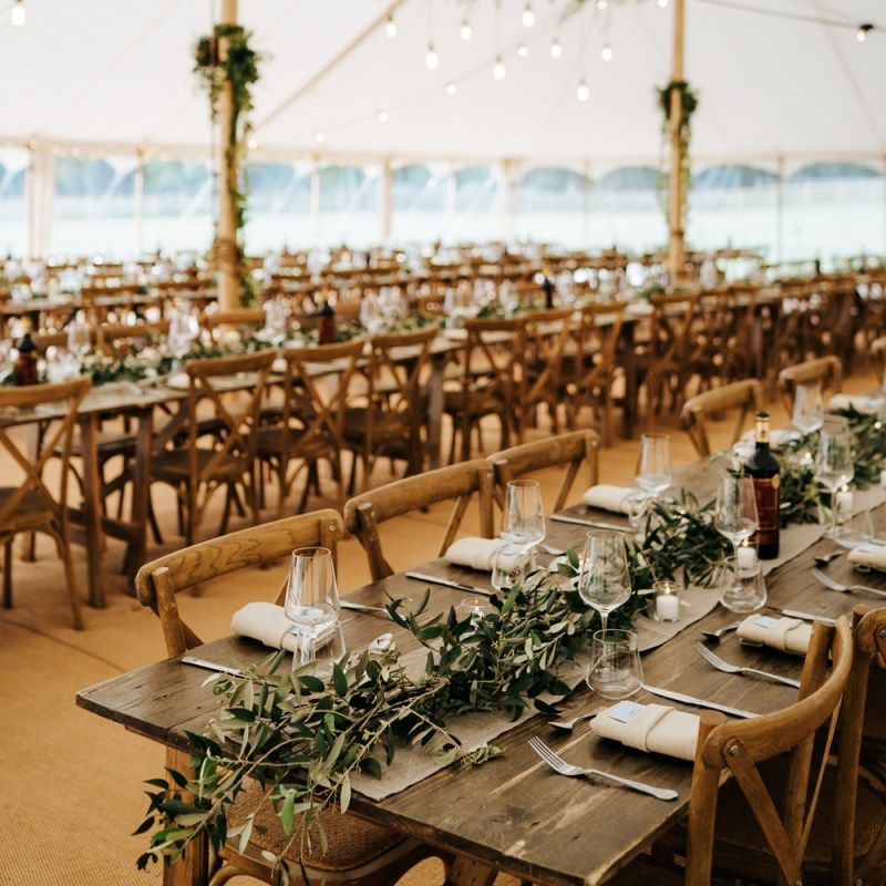 Marquee reception with wooden tables, greenery table runners and hanging festoon lights