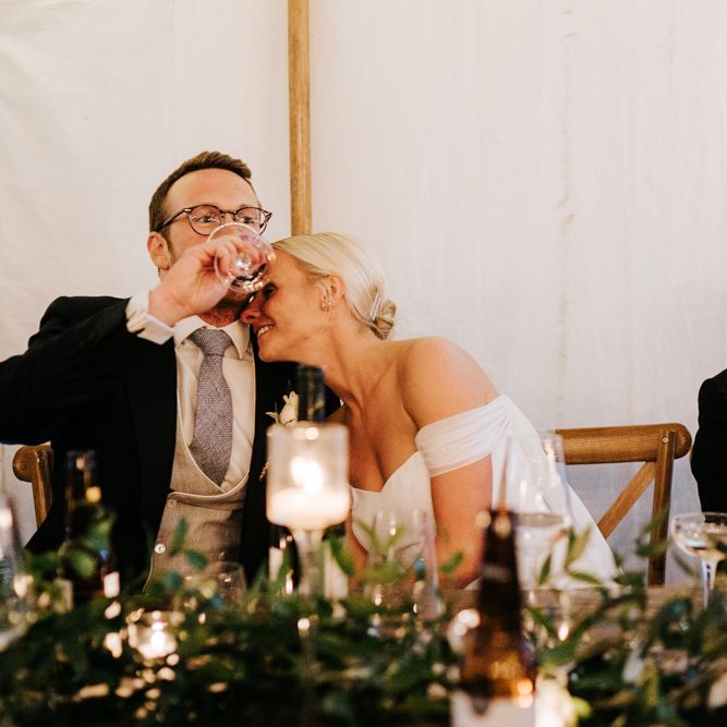 Bride embraces groom, as he takes a drink of wine, after he has completed his speech