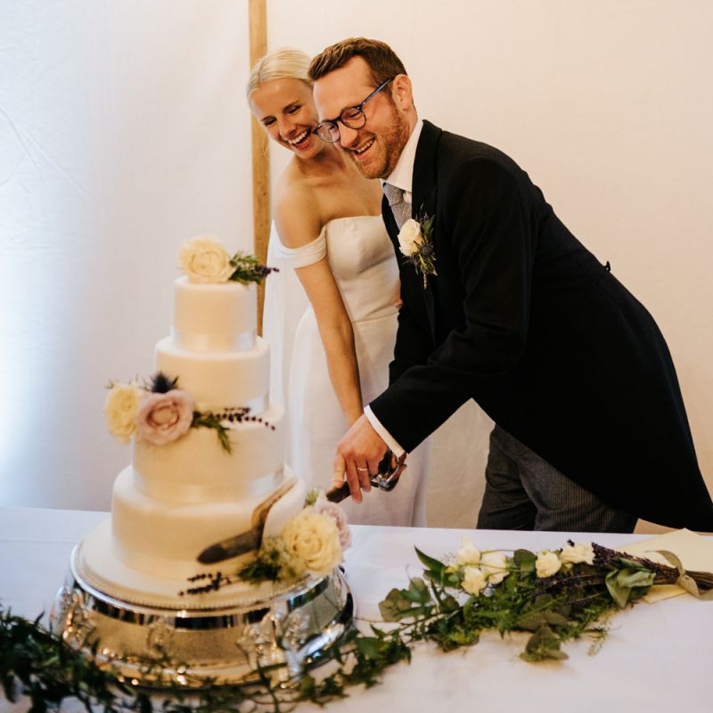 Bride and groom smile as they cut the wedding cake with a sword