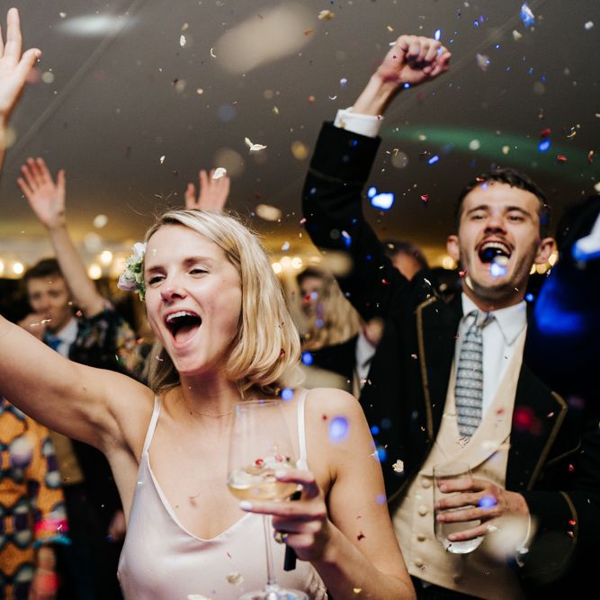 Sister of the bride and guests smiling and cheering as confetti explodes over the dancefloor