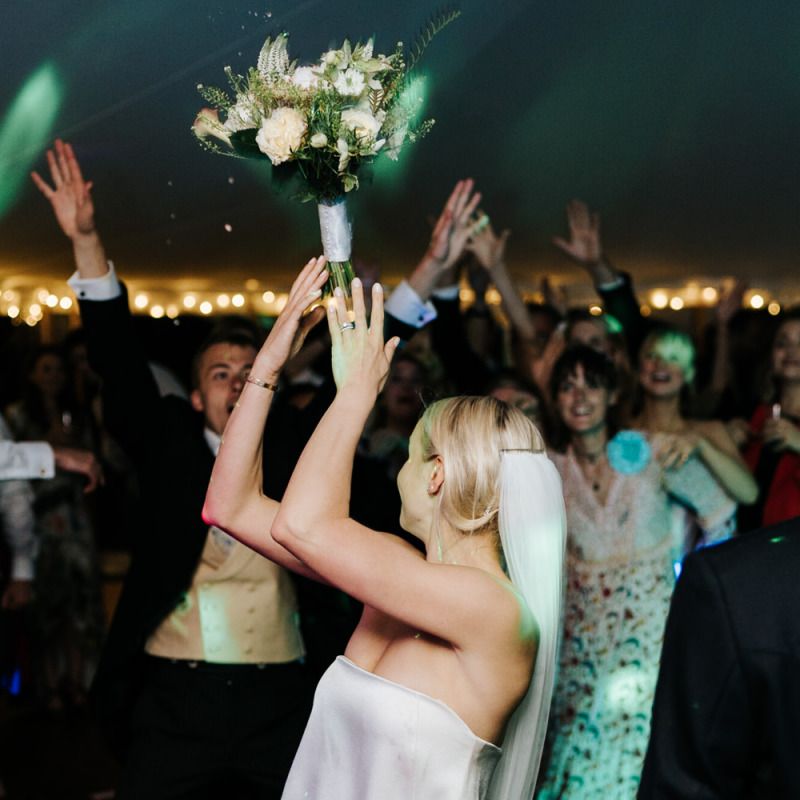 Bride throws bouquet into crowd of keen guests on the dancefloor