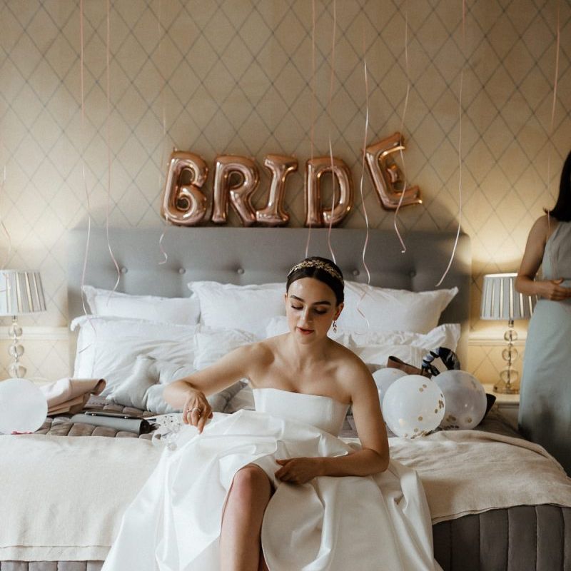 Bride In Strapless Wedding Dress Puts On Shoes With Wedding Balloons