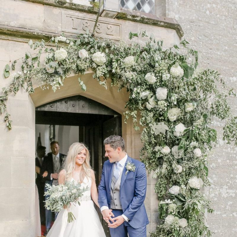 Bride in Sassi Holford wedding dress and groom in classic suit exiting the church