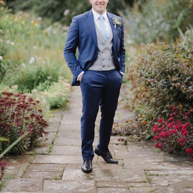 Groom in Navy suit with grey waistcoat standing in aAskham Hall  gardens