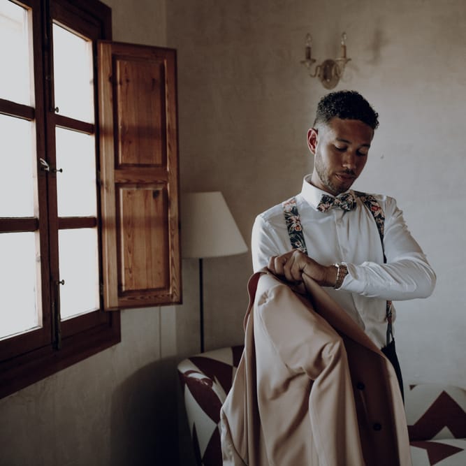 Groom getting ready on wedding morning with floral braces and bow ties