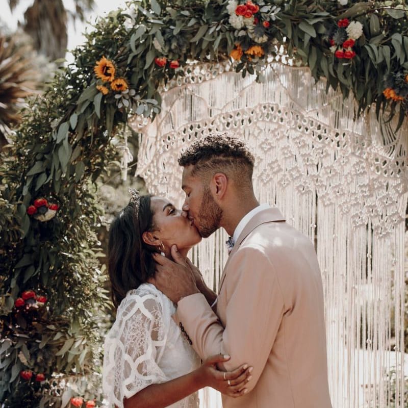 Groom on pale pink blazer kissing his bride in a Grace Loves Lace wedding dress