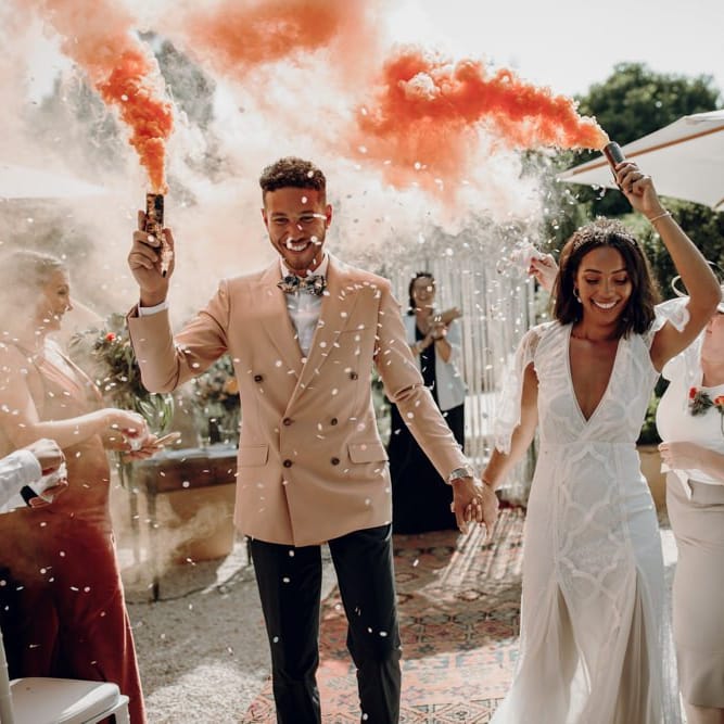Boho bride and groom holding orange smoke bombs