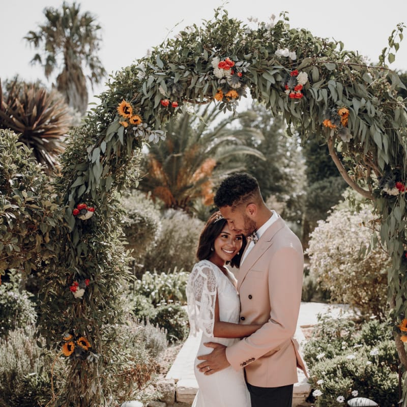 Bride and groom embracing under a floral arch