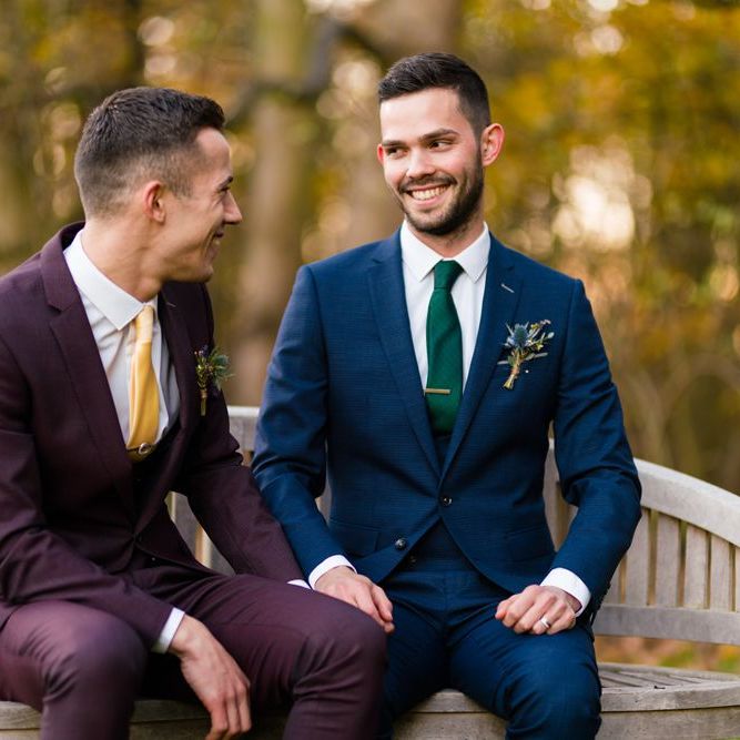Two Grooms in Burgundy and Navy Remus Uomo Suits Sitting on a Bench