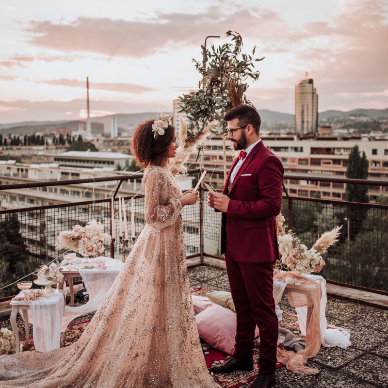 Bride and groom exchanging vows on a rooftop in sparkle wedding dress and burgundy suit