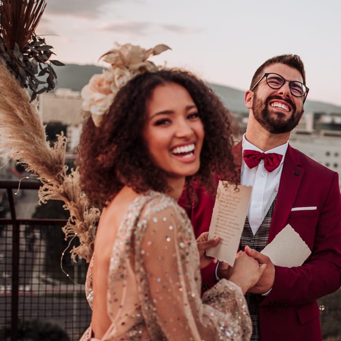Groom in red suit and bow tie laughing during intimate wedding ceremony