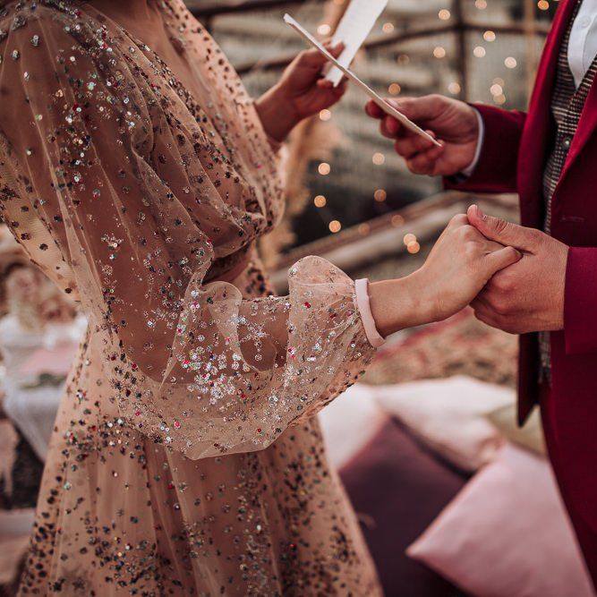 Bride in nude tulle and sparkle wedding dress holding hands with her husband during the wedding ceremony