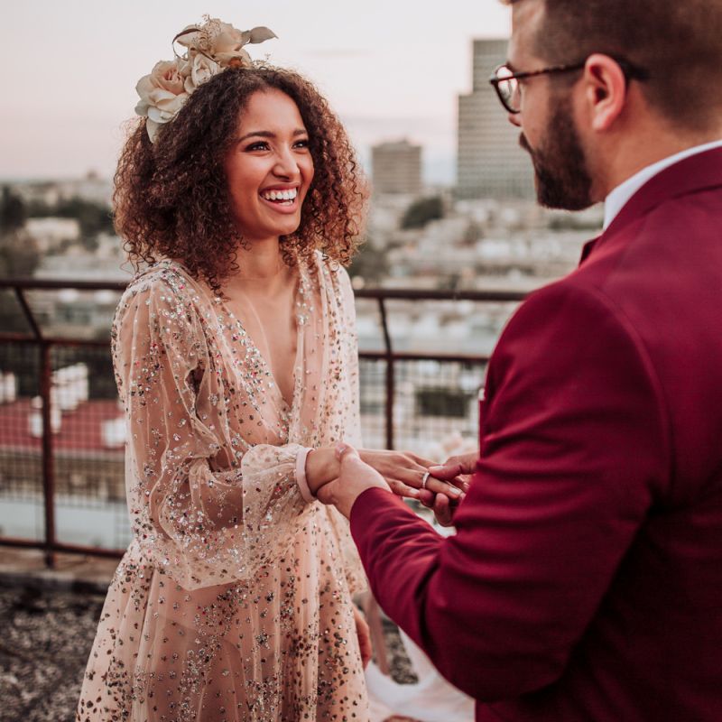 Bride in sparkle wedding dress smiling as her groom puts on her wedding ring