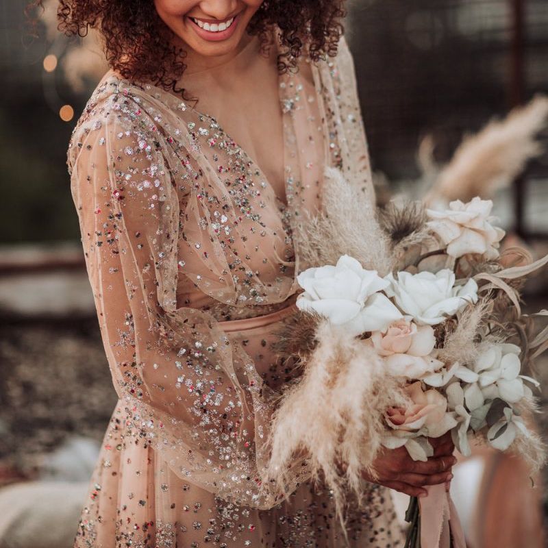 Boho bride in sparkle wedding dress with long sleeves and flowers in her curly hair