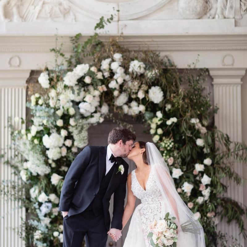 Bride and groom kiss in front of beautiful white floral hoop decor