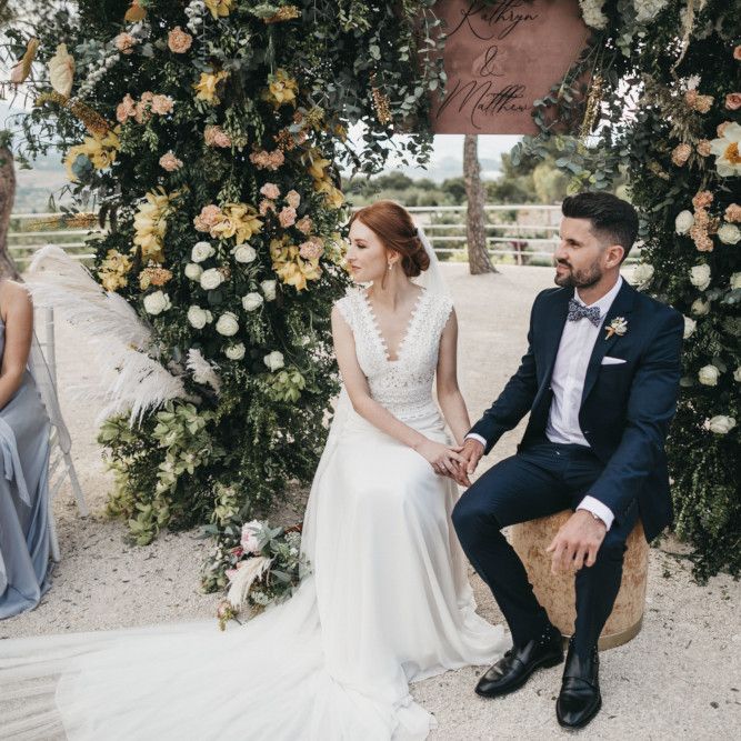 Bride and Groom Holding Hands During the Wedding Ceremony with a Floral Arch Backdrop
