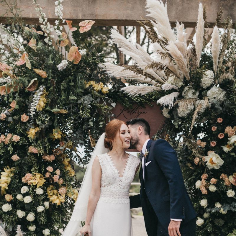 Groom in Navy Tuxedo Kissing His Bride on the Cheek During the Wedding Ceremony