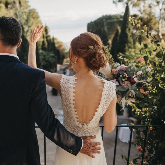 Bride in Backless Pronovias Wedding Dress and Groom in Navy Suit Waving to Their Wedding Guests on the Balcony