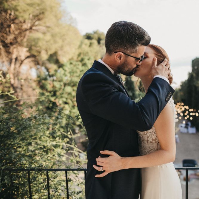 Groom in Navy Suit Kissing His Bride on the Balcony