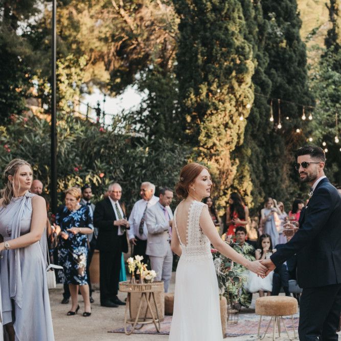 Bride in Pronovias Wedding Dress and Groom in Navy Suit Holding Hands at the Wedding Reception
