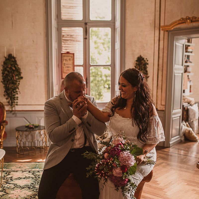 Groom in Grey Blazer and Bow Tie Kissing His Brides Hand in an Off The Shoulder Wedding Dress