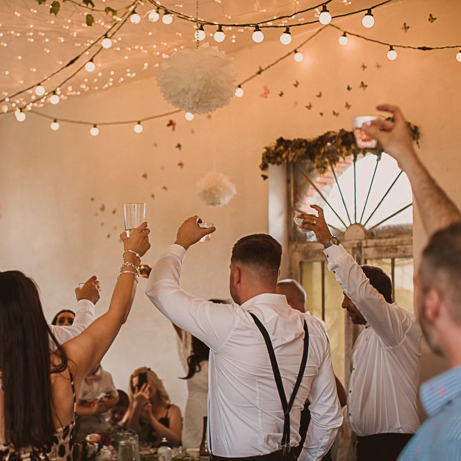 Wedding Guests Raising a Glass in the Festoon Lit Wedding Reception
