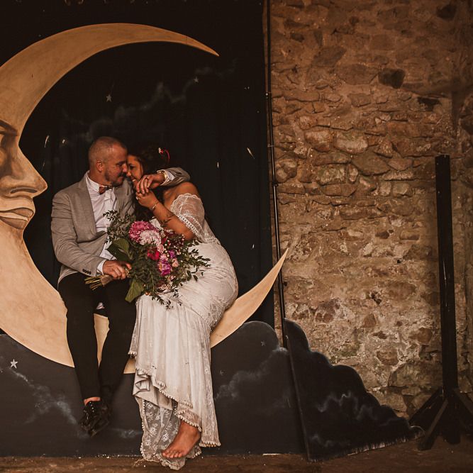 Bride in Emanuela Grace Loves Lace Wedding Dress and Groom in Grey Blazer Embracing on a Giant Moon