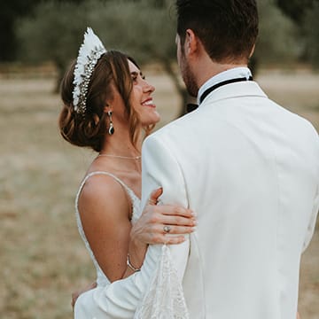 Bride Wears Feather Headdress And Gazes At Husband In White Dinner Jacket