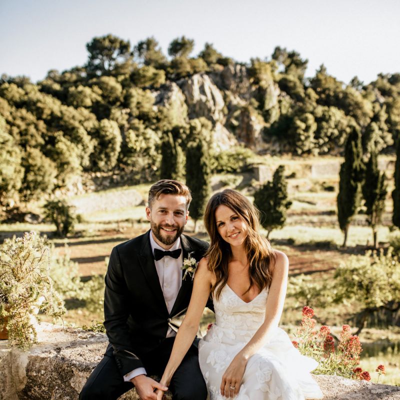 Bride in Tiered Lace Emma Beaumont Wedding Dress and Groom in Givenchy Tuxedo Sitting Hand in Hand