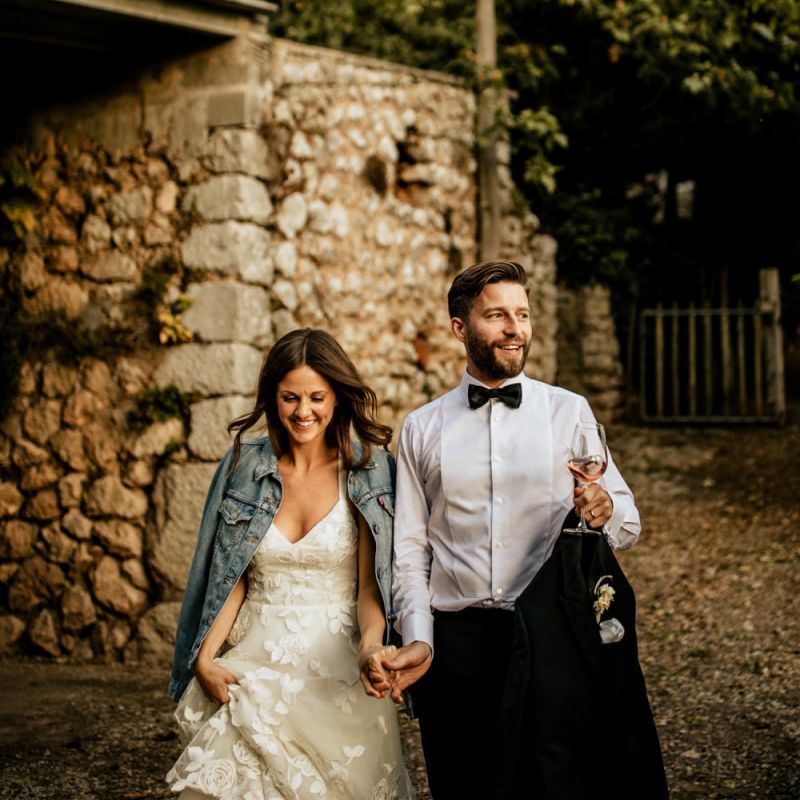 Bride in Emma Beaumont Wedding Dress and Denim Jacket and Groom in Givenchy Tuxedo Holding Hands