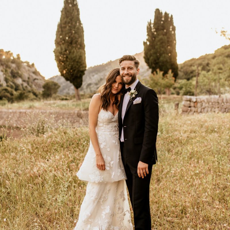 Bride in Tiered Lace Emma Beaumont Wedding Dress and Groom in Givenchy Tuxedo Embracing