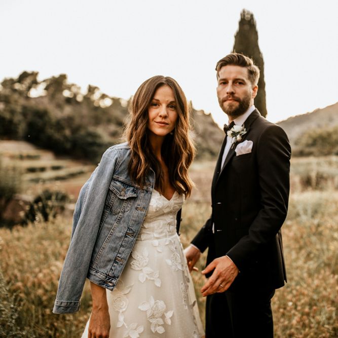 Bride in Tiered Lace Emma Beaumont Wedding Dress and Blue Denim Jacket and Groom in Givenchy Tuxedo
