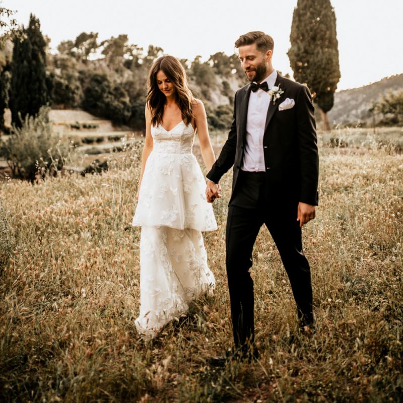 Bride in Tiered Lace Emma Beaumont Wedding Dress and Groom in Givenchy Tuxedo Holding Hands