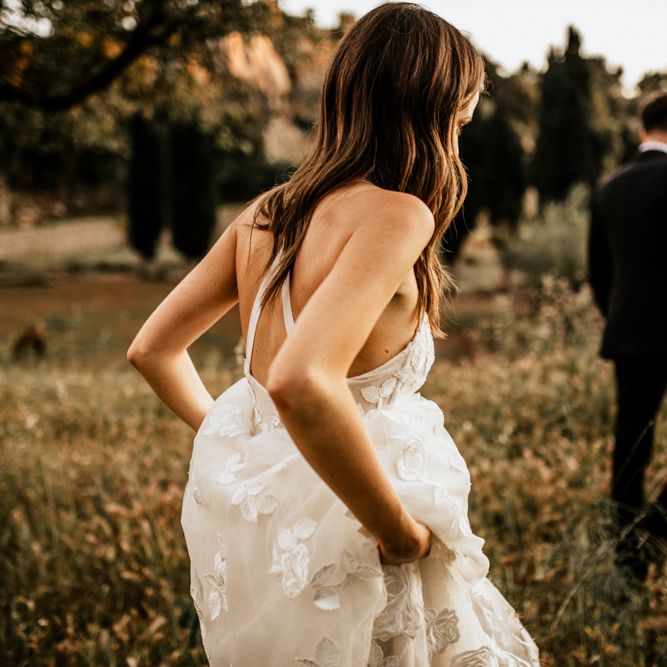 Bride Holding Her Tiered Lace Emma Beaumont Wedding Dress  Up Walking Through Fields