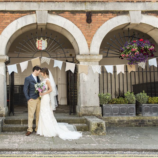 Bride in Lacy Fishtail Stella York Gown with Plunging V Back and Diamante Charm on Champagne Ribbon Belt | Summer Bridal Bouquet with Purple and Blue Flowers and Eucalyptus | Groom in Blue Jacket and Waistcoat with Camel Chinos | Giant Pastel Bunting Flags | Wedding Ceremony at Rye Town Hall | Morris Minor Wedding Car, Hanging Flowers in Bottles and Town Crier for Village Hall Wedding in Rye | Eleanor Jane Photography