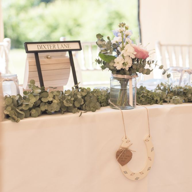 Eucalyptus Top Table Runner | Road Sign Table Names | Horseshoe Decoration | Pink, Blue and White Flowers in Glass Jar | Tipi Wedding Reception at Udimore Village Hall, East Sussex | Morris Minor Wedding Car, Hanging Flowers in Bottles and Town Crier for Village Hall Wedding in Rye | Eleanor Jane Photography