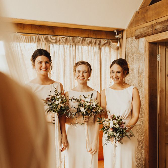 Bridesmaids in blush dresses see bride in wedding dress for first time