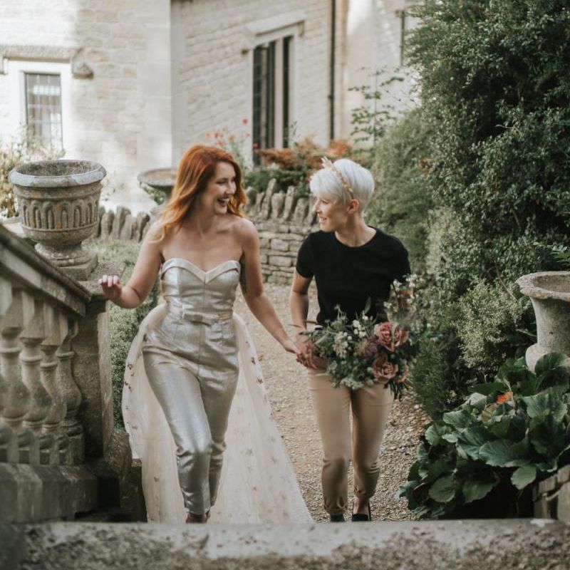 Bride in gold jumpsuit and bride in black t shirt and beige trousers