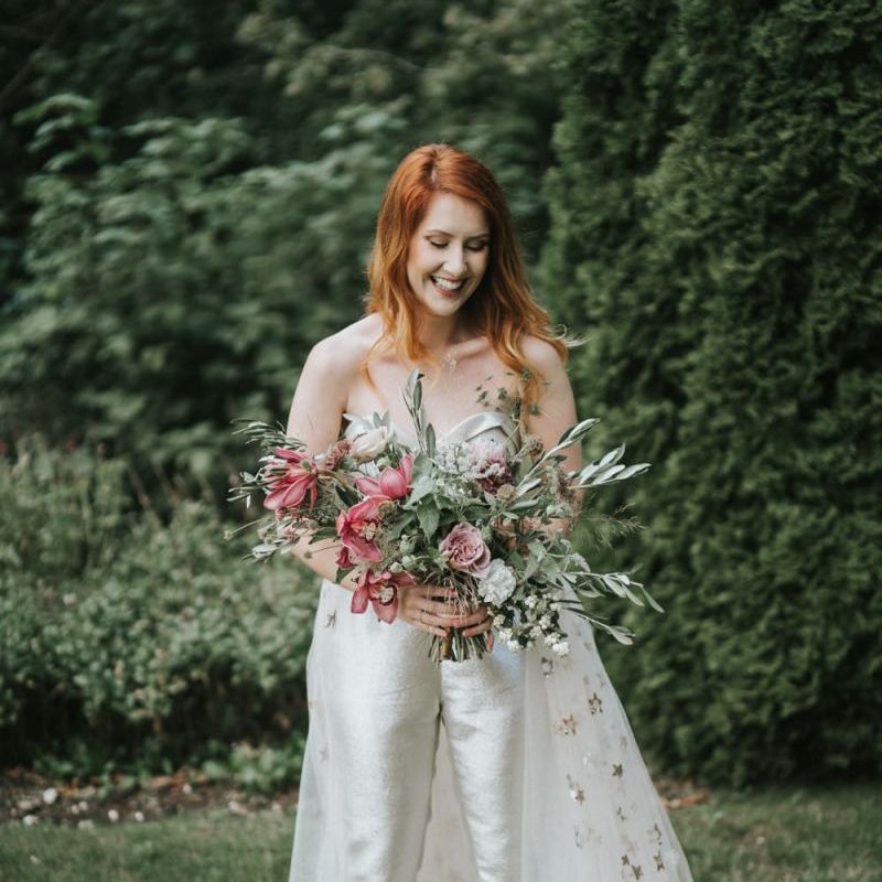 Bride in strapless bridal jumpsuit holding a romantic wedding bouquet