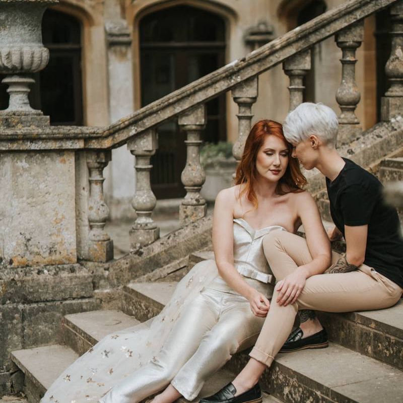 Brides sitting on the steps at Castle Combe Manor House in Wiltshire for LGBTQ+ wedding