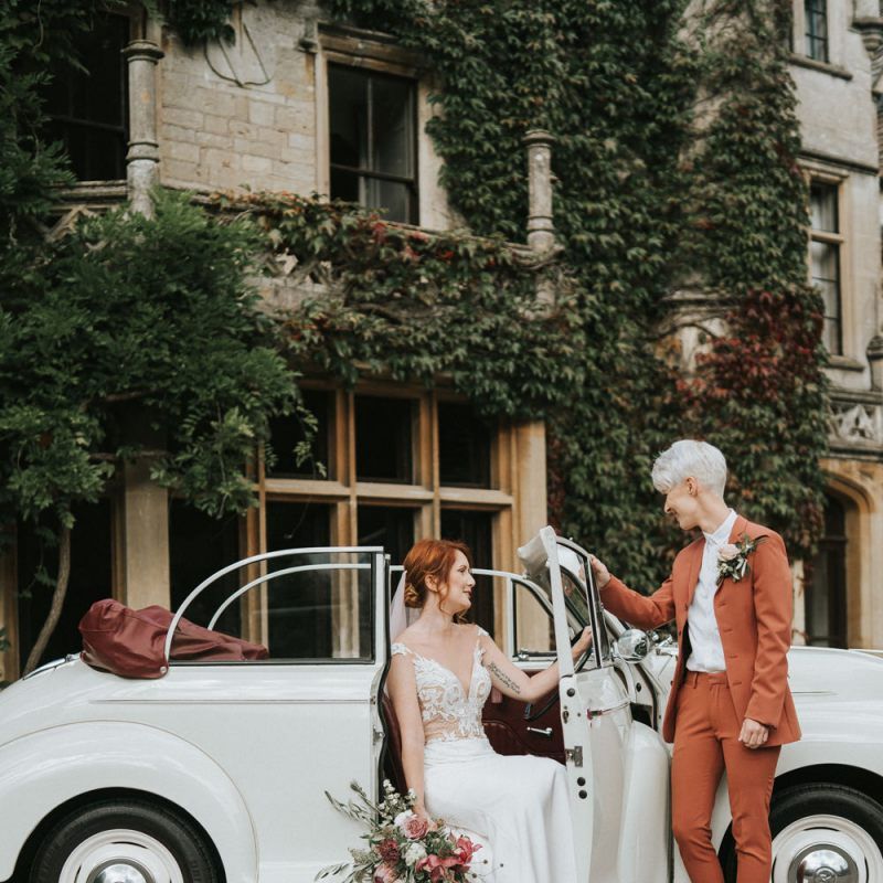 Bride with short hair in suit and trainers and bride in lace wedding dress sitting in a wedding cake