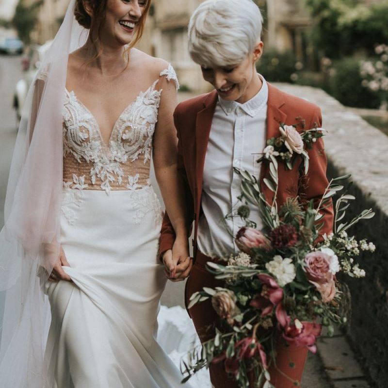 Brides holding hands walking through picturesque Wiltshire village