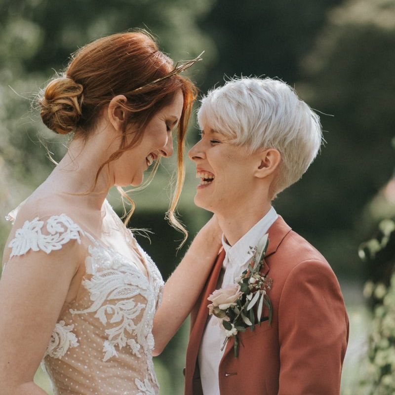 Bride in lace wedding dress and bride in rust coloured suit