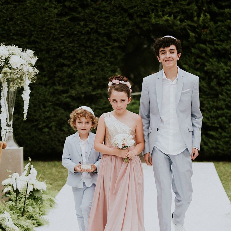 Bridesmaid and page boys walk down the aisle at Jewish wedding ceremony