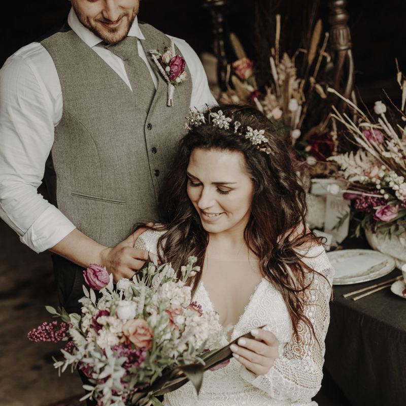 Boho Bride in Lace Wedding Dress Looking at White and Purple Wedding Bouquet