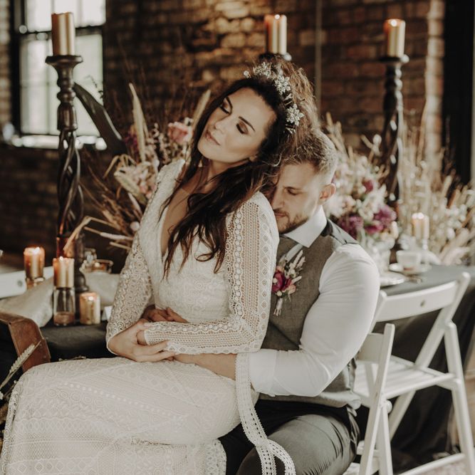 Boho Bride in Lace Wedding Dress and Groom in Wool Waistcoat Sitting at Rustic Tablescape with Dried Flower Decor and Floral Tableware