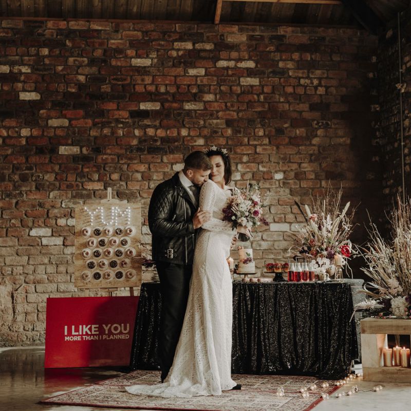 Boho Bride in Lace Wedding Dress and Groom in Leather Jacket Standing at Dessert Table