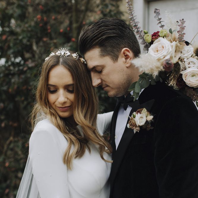 Bride in Emma Beaumont Wedding Dress and Tilly Thomas Lux Headdress and Groom in Tuxedo Embracing