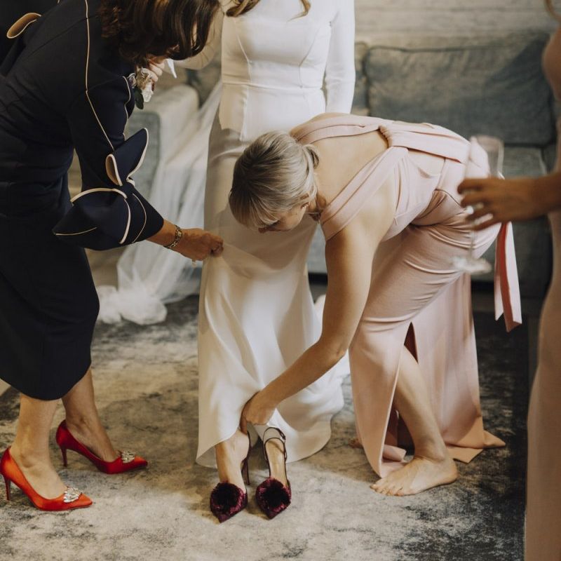 Bride Putting on Burgundy Pom Pom Wedding Shoes